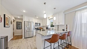 A modern kitchen with white cabinets, stainless steel appliances, and a large island with bar stools.