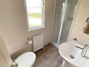 A bathroom with a toilet, a sink, a glass shower enclosure, and a window.