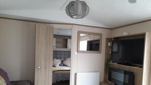A modern living room with a sofa, a coffee table, a TV, and a bed with a headboard. - Impeccable 3-bed Cabin in Tattershall, UK (Lincoln)