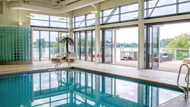 An indoor swimming pool with clear glass walls, a lounge area with chairs, and a view of the outdoors. - Impeccable 3-bed Cabin in Tattershall, UK (Lincoln)