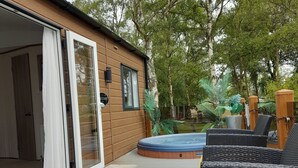 A wooden cabin with a glass door, a hot tub, and wicker furniture. - Impeccable 3-bed Cabin in Tattershall, UK (Lincoln)