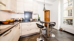 A modern kitchen with white cabinets, a black countertop, and a bar stool. - THE FRENCH CAPITAL ABODE;LOUVRE , TUILERIES, PLACE VENDOME (Paris)