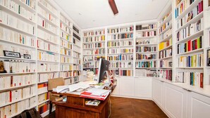 A library with white bookshelves filled with books, a wooden desk with papers, and a computer monitor. - THE FRENCH CAPITAL ABODE;LOUVRE , TUILERIES, PLACE VENDOME (Paris)