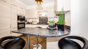 A modern kitchen with a granite countertop, stainless steel appliances, and a central island with bar stools. - THE FRENCH CAPITAL ABODE;LOUVRE , TUILERIES, PLACE VENDOME (Paris)