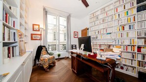 A library with bookshelves, a desk with a computer, and a window with a view. - THE FRENCH CAPITAL ABODE;LOUVRE , TUILERIES, PLACE VENDOME (Paris)