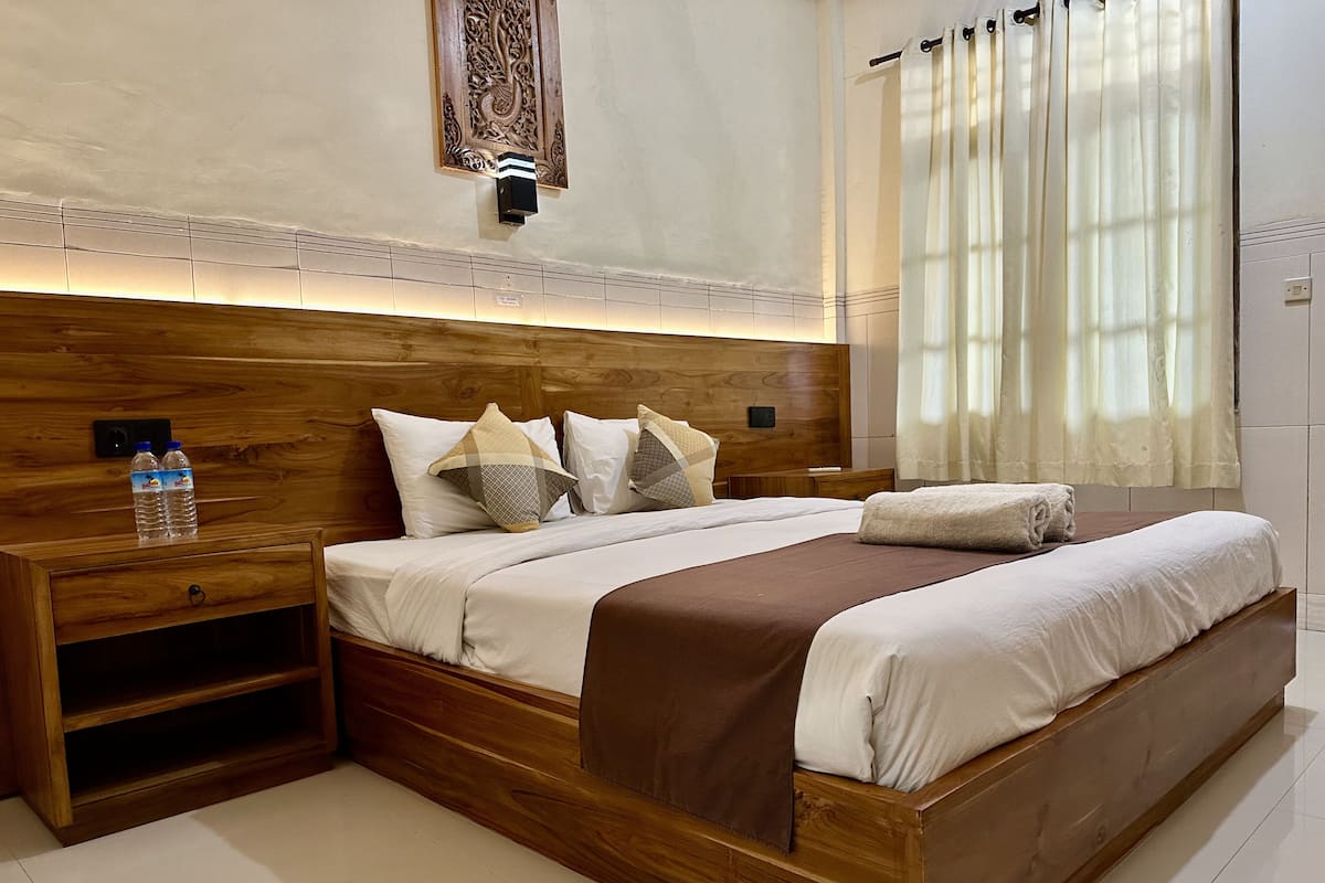 Ein modernes Schlafzimmer mit einem Holz-Kopfteil, einem Nachttisch mit einer Wasserflasche, einem großen Bett mit einer braunen Tagesdecke und einem dekorativen Wandbild darüber.