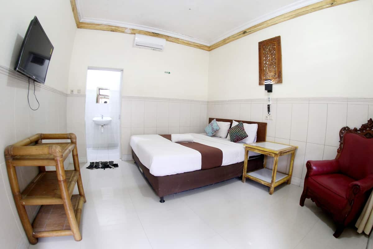 Ein Hotelzimmer mit einem Bett, einem roten Sessel, einem Holztischchen, einem Fernseher und einem durch eine offene Tür einsehbaren Badezimmer.