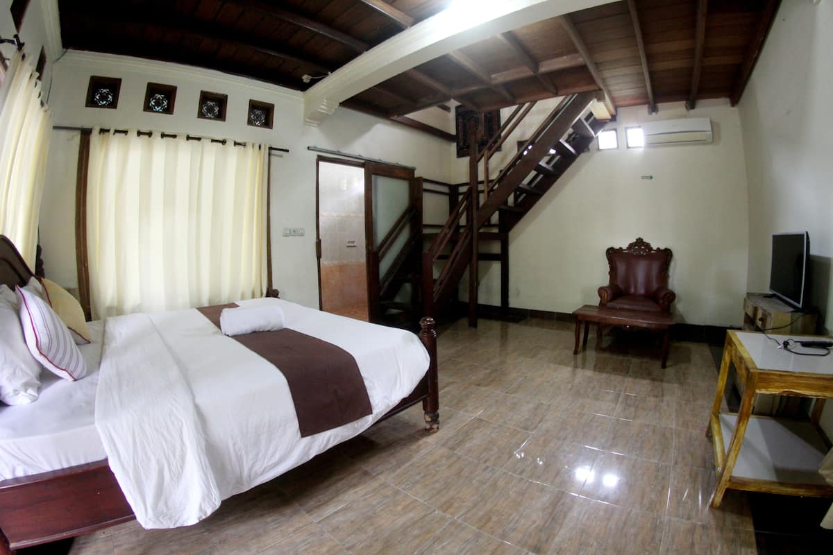 Ein Schlafzimmer mit Bett, Sessel, Schreibtisch, Fernseher und einer Treppe.