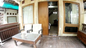 A room with a glass-top table and two chairs, a wooden bench, and a view of a corridor with a bed and a door. - GILI BEACH WIND (Gili Trawangan)