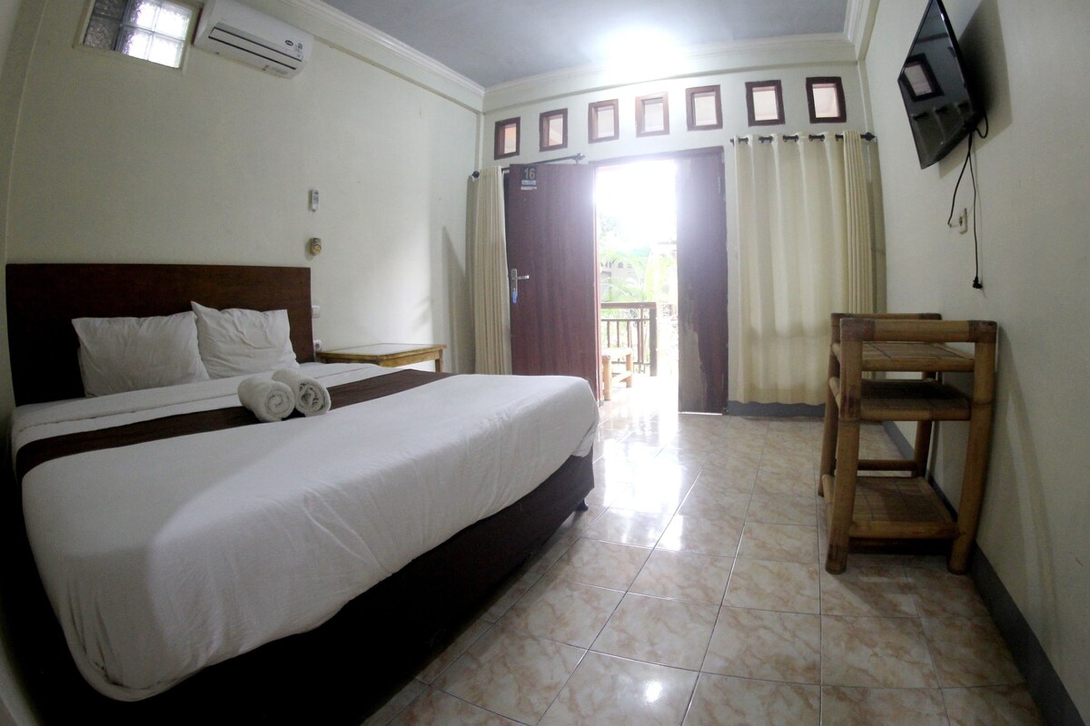 A hotel room with a bed, a TV mounted on the wall, and a balcony door.