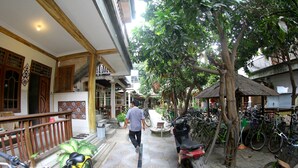 A courtyard with a tiled floor, bicycles, and a man walking. - GILI BEACH WIND (Gili Trawangan)