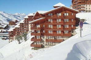 A multi-story wooden building with balconies, set against a snowy mountain backdrop.