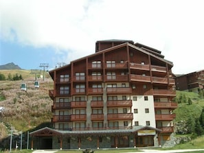 A multi-story hotel with balconies, a ski lift in the background, and a mountainous landscape. - 10m from ski slopes, Ground floor, view mountain, balcony, tv, ski locker, 40m², Les Menuires (Les Menuires)