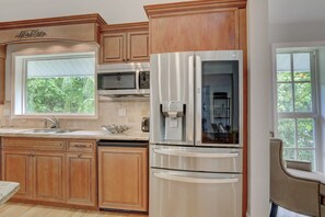 Una cocina con armarios de madera, un refrigerador de acero inoxidable, un microondas y una ventana con vista a la vegetación.