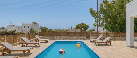 A swimming pool with lounge chairs, a beach ball, and a view of the sea.
