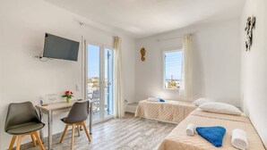 Una camera d'albergo con un letto, una scrivania, due sedie, una televisione e vista sul mare.