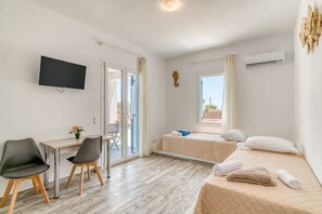 A hotel room with a bed, a desk, two chairs, a TV, and a window. - Paros Poolside Getaway - Artemis Beach House (Aliki)