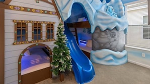 A children's play area with a slide, a small Christmas tree, and a wall mural of a snowy mountain.
