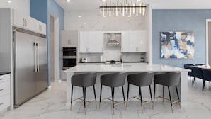 A modern kitchen with a central island, bar stools, stainless steel appliances, and a contemporary light fixture.