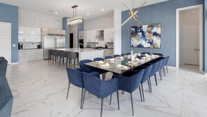 A modern kitchen with white cabinets, a central island, and a dining area with blue chairs and a glass table.