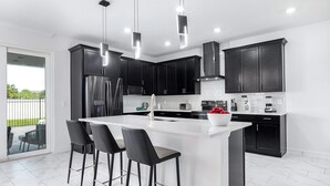 A modern kitchen with dark cabinets, a large island with bar stools, stainless steel appliances, and pendant lighting. - The Sea Renity | Relax & Rejuvenate in This Picturesque Retreat, Mins From Beach (Melbourne Beach)