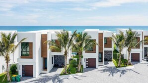A modern hotel with multiple white buildings, palm trees, and a view of the ocean.