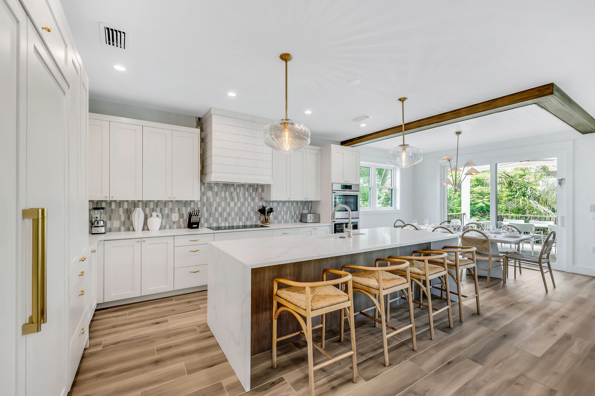 A modern kitchen with white cabinets, a large island with bar stools, and a view of the outdoors.