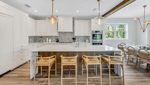 A modern kitchen with white cabinetry, a large island with bar stools, and pendant lighting.