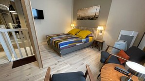 A hotel room with a bed, a desk, a chair, a TV, and a painting on the wall. - Quartier Voltaire - Rue Pache (Paris)