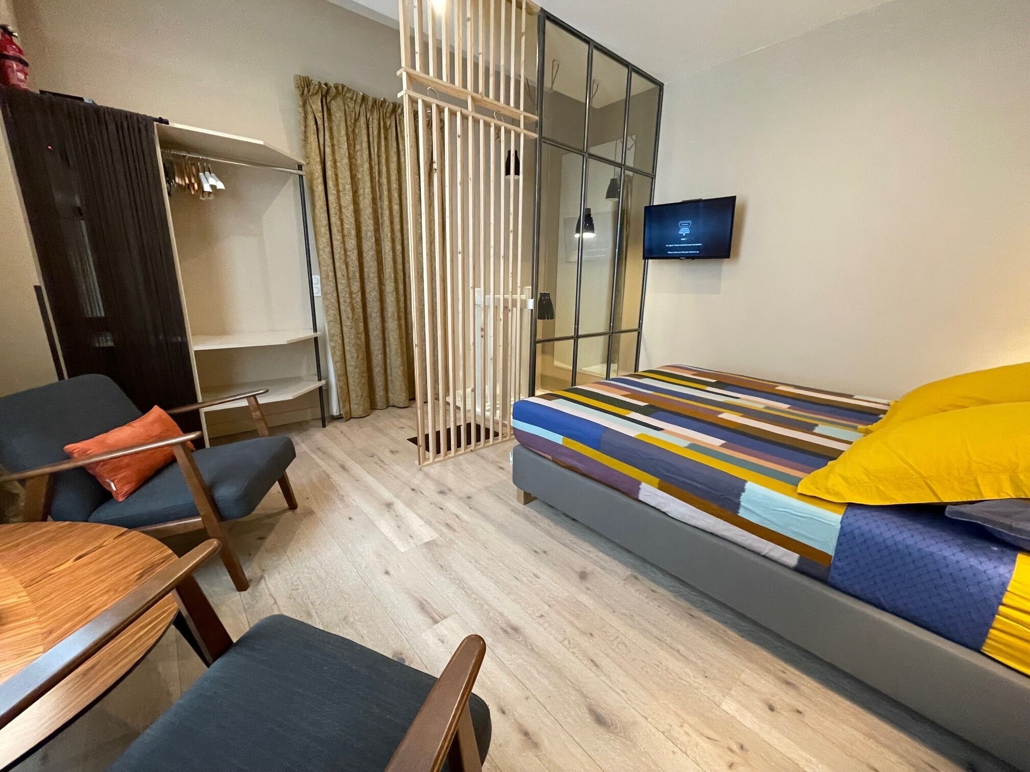 A modern hotel room with a bed, a desk, a chair, a wardrobe, and a television.