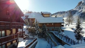 A snow-covered building with a balcony, a staircase leading to a covered area, and a view of snow-covered trees and mountains in the background. - 1st floor, terrace, parking, tv, 60m², Saint Martin de Belleville (Saint-Martin-de-Belleville)