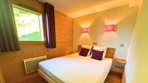 A bedroom with a large bed, wooden walls, a window with curtains, and two wall-mounted lights. - 1st floor, terrace, parking, tv, 60m², Saint Martin de Belleville (Saint-Martin-de-Belleville)