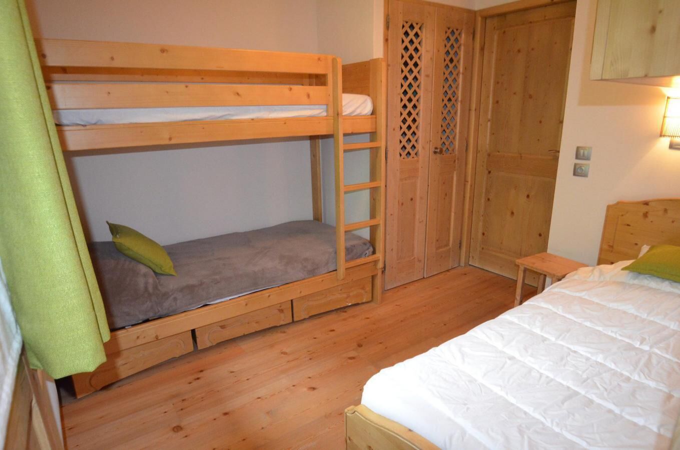 Een slaapkamer met stapelbedden, een houten vloer, een tafeltje en een garderobe met een rankenpatroon.