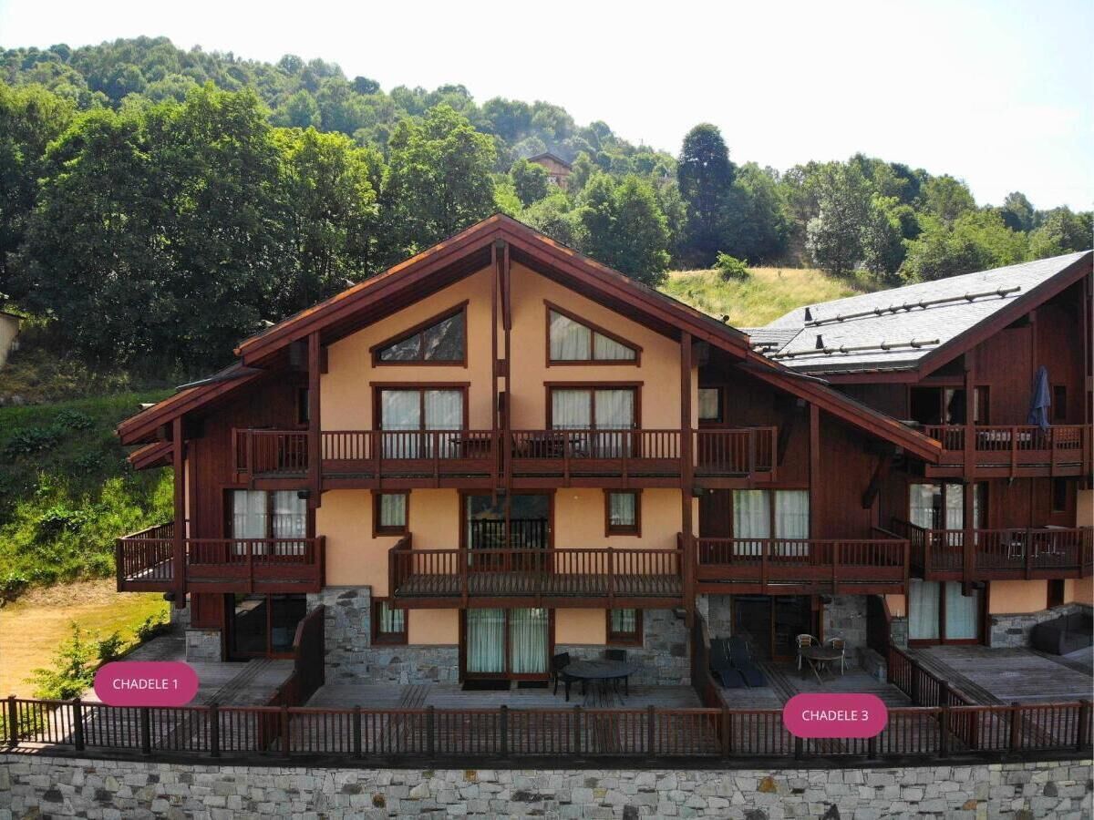 Ein mehrgeschossiges Chalet mit Balkonen, einem Steinfundament und Blick auf einen bewaldeten Hang.