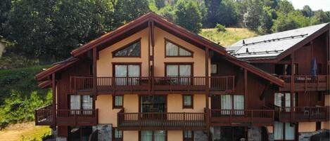 Ein mehrgeschossiges Chalet mit Balkonen, einem Steinfundament und Blick auf einen bewaldeten Hang.