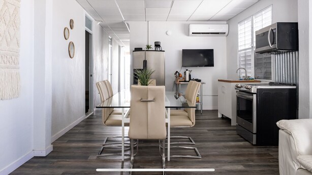 A modern kitchen with a dining area, featuring a flat-screen TV, stainless steel appliances, and a minimalist design.