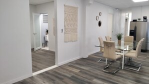 A modern office space with a glass table and chairs, a refrigerator, and a wall-mounted clock.