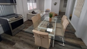 A modern living room with a glass dining table, beige sofas, a built-in oven, and a TV.