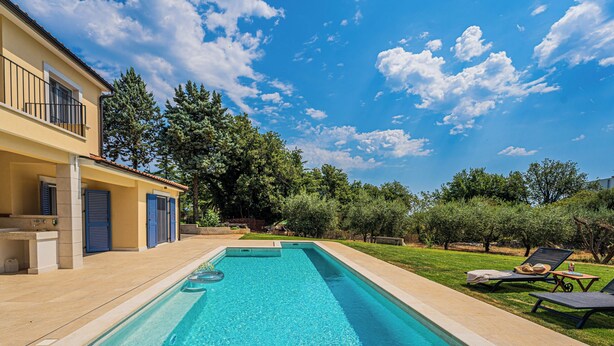Una piscina rectangular con superficie de agua azul cristalina, rodeada por un solárium empedrado.