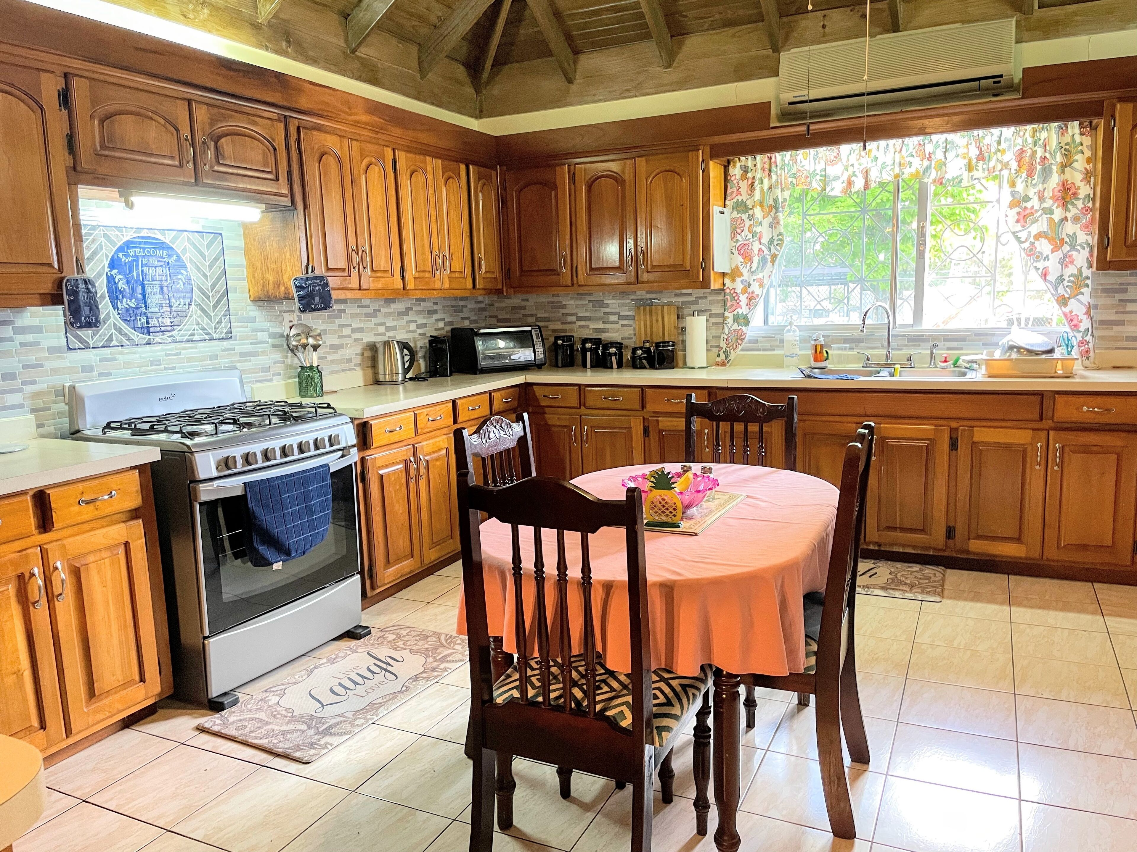 Una cocina con armarios de madera, cocina a gas, microondas y comedor con mesa y sillas.
