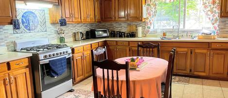 Una cocina con armarios de madera, cocina a gas, microondas y comedor con mesa y sillas.