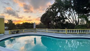 A swimming pool with a white balustrade, surrounded by trees and a sunset in the background. - Yancey Largo Villa Perfect Jamaica Ironshore Getaway w Private Pool and Onsite Staff Services by RedAwning (Montego Bay)