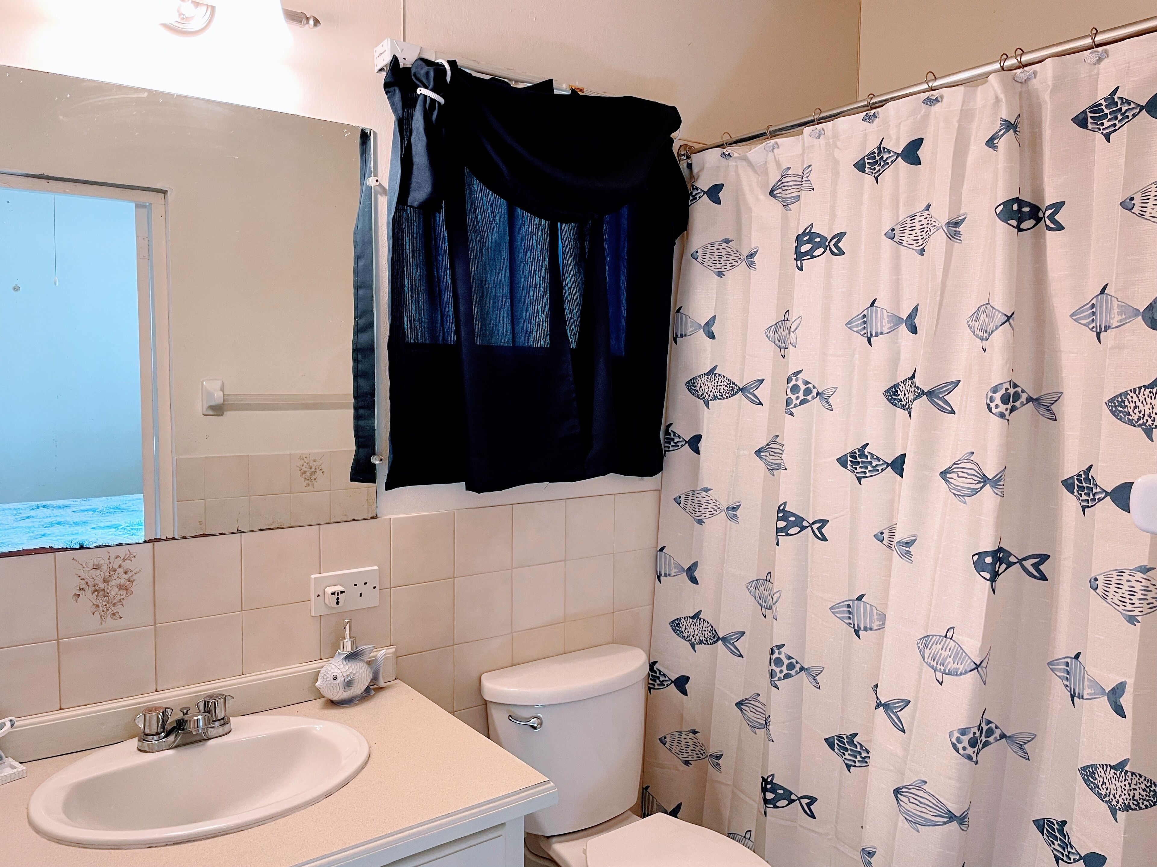 A bathroom with a sink, toilet, and shower curtain with a fish pattern.