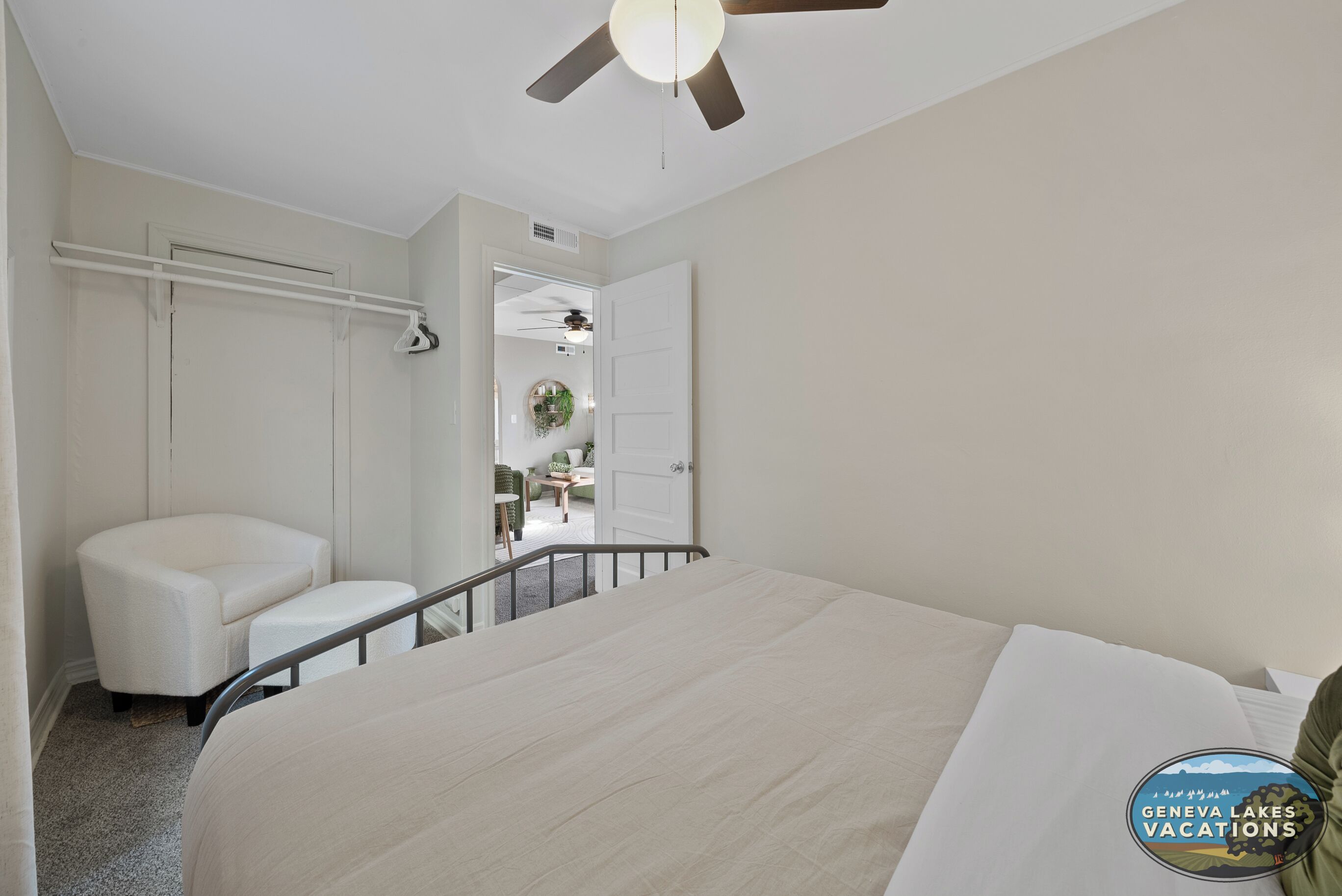 Une chambre à coucher comprenant un lit, une chaise, un ventilateur de plafond et un couloir menant à une autre pièce.