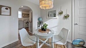 A dining area with a glass table, two white chairs, a woven placemat, and a hanging light fixture. - Broad Street Suites 1,2 & 3 |Sleeps 20 |Parking for 7 Vehicles |Downtown |Events |Horticultural Hall (Lake Geneva)