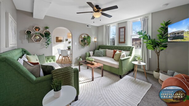 A modern living room with a green sofa, a white coffee table, and a ceiling fan. - Broad Street Suites 1,2 & 3 |Sleeps 20 |Parking for 7 Vehicles |Downtown |Events |Horticultural Hall (Lake Geneva)
