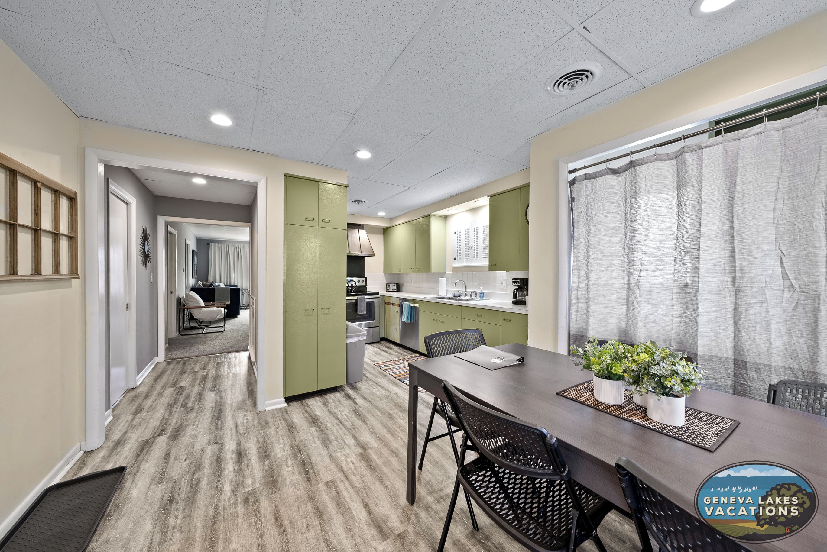 Una cocina moderna con gabinetes verdes, un comedor con mesa y sillas, y vistas a un lago.