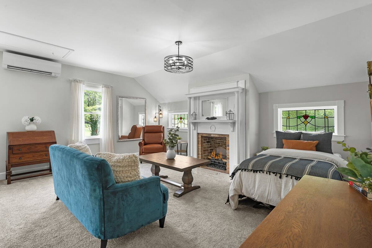 A spacious room with a fireplace, a large window with a view, a blue armchair, and a wooden table.