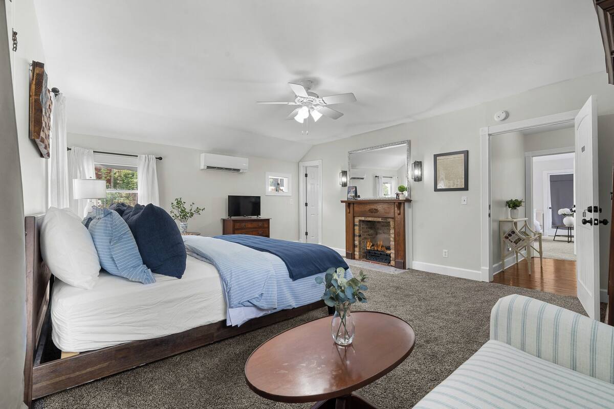 A bedroom with a bed, a TV, a fireplace, and a ceiling fan.