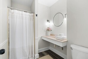 Een badkamer met douchegordijn, wastafel met bloemenvaas, spiegel en toilet.